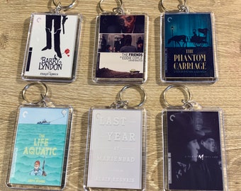 May include: Six keychains with clear plastic frames and silver rings. Each keychain features a different movie poster. The posters include "Barry Lyndon", "The Friends of Eddie Coyle", "The Phantom Carriage", "The Life Aquatic", "Last Year at Marienbad", and "M" by Fritz Lang.
