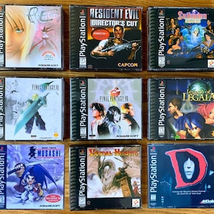 Pode incluir: Nove caixas de jogos PlayStation são exibidas, cada uma com uma borda preta e uma lombada azul com o logotipo PlayStation. As capas dos jogos apresentam diversas obras de arte, incluindo personagens, cenas de ação e títulos de jogos.