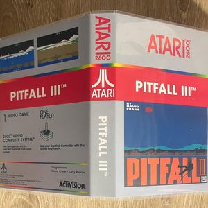 May include: A boxed Atari 2600 video game cartridge for Pitfall III. The box is gray with red accents and features game screenshots, the Atari logo, and the game title. The box is sealed in clear plastic.
