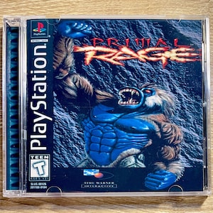 May include: A PlayStation game case for "Primal Rage." The cover art shows a blue gorilla-like creature with a menacing expression, set against a dark, textured background. The game's title is in fiery orange letters. The case is in a clear plastic jewel case.