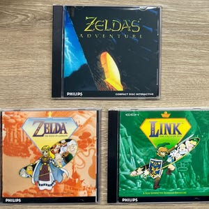 May include: Three CD-ROM game cases featuring the Zelda series. The top case is titled "Zelda's Adventure" with a dark background and yellow accents. The bottom left case is "Zelda The Wand of Gamelon". The bottom right case is "Link The Faces of Evil".