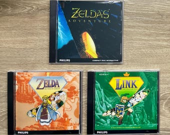 May include: Three CD-ROM game cases featuring the Zelda series. The top case is titled "Zelda's Adventure" with a dark background and yellow accents. The bottom left case is "Zelda The Wand of Gamelon". The bottom right case is "Link The Faces of Evil".