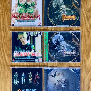 May include: Four PlayStation game cases with the titles "Metal Gear Solid", "Castlevania Symphony of the Night", "Silent Hill", and "Castlevania Symphony of the Night". The cases are on a wooden surface.