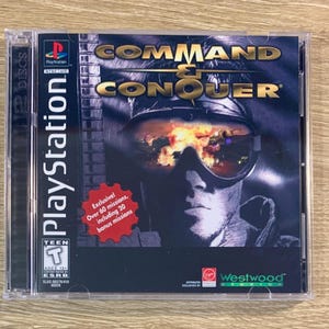May include: A PlayStation game case for Command & Conquer, featuring a soldier wearing goggles and a dark jacket. The case is black with a red and white design. The text "Exclusive! Over 60 missions, including 20 bonus missions" is printed on the case.