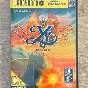 May include: A TurboGrafx-16 CD game case for "Ys Book I & II." The cover art shows a fantasy scene with a winged figure, a castle, and the game's title. The case has a yellow top banner with the TurboGrafx logo and the text "CD Graphics".