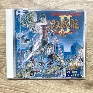 May include: A Double Dragon II: The Revenge PC Engine game case. The cover art features a dynamic illustration of characters in action, with the title in English and Japanese. The case is in a clear plastic sleeve.