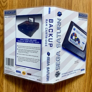 May include: Sega Saturn Backup RAM cartridge, with a blue and white design and the Sega Saturn logo. The packaging includes text that reads "Save Games and Keep Track of Your Teams' Stats."