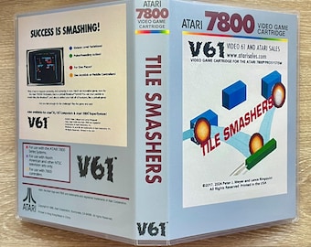 Könnte beinhalten: Eine durchsichtige Kunststoffhülle für ein Atari 7800 Videospielmodul mit dem Titel Tile Smashers. Das Cover zeigt blaue Blöcke, orangefarbene Kugeln und ein grünes Paddel. Die Rückseite enthält den Text Success Is Smashing und V61.
