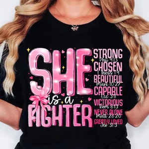 May include: Black t-shirt with the words "SHE is a FIGHTER" in pink, along with other words like "STRONG" and "CHOSEN". The design includes a pink bow and sparkles.