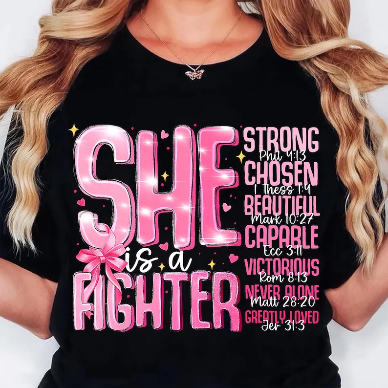 May include: Black t-shirt with the words "SHE is a FIGHTER" in pink, along with other words like "STRONG" and "CHOSEN". The design includes a pink bow and sparkles.