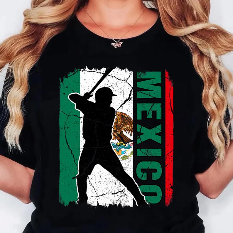 May include: Black t-shirt with a baseball player silhouette holding a bat, set against a distressed Mexican flag design. The word "MEXICO" is vertically printed in green and red. The shirt has a crew neck.
