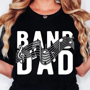 K&ouml;nnte beinhalten: Schwarzes T-Shirt mit dem wei&szlig;en Schriftzug "BAND DAD". Zwischen den W&ouml;rtern befindet sich ein wei&szlig;es Notensystem mit Noten. Der Violinschl&uuml;ssel ist auf der linken Seite zu sehen.