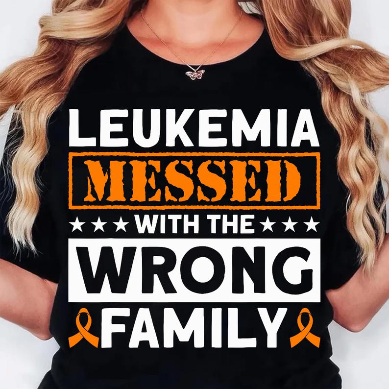 May include: Black t-shirt with the text "LEUKEMIA MESSED WITH THE WRONG FAMILY" in white and orange. The design includes orange awareness ribbons and stars. The shirt is a crew neck.
