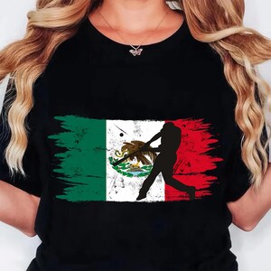 May include: Black t-shirt with a Mexican flag design and a baseball player silhouette. The flag is in green, white, and red with a brushstroke effect. The baseball player is in mid-swing, creating a dynamic image.