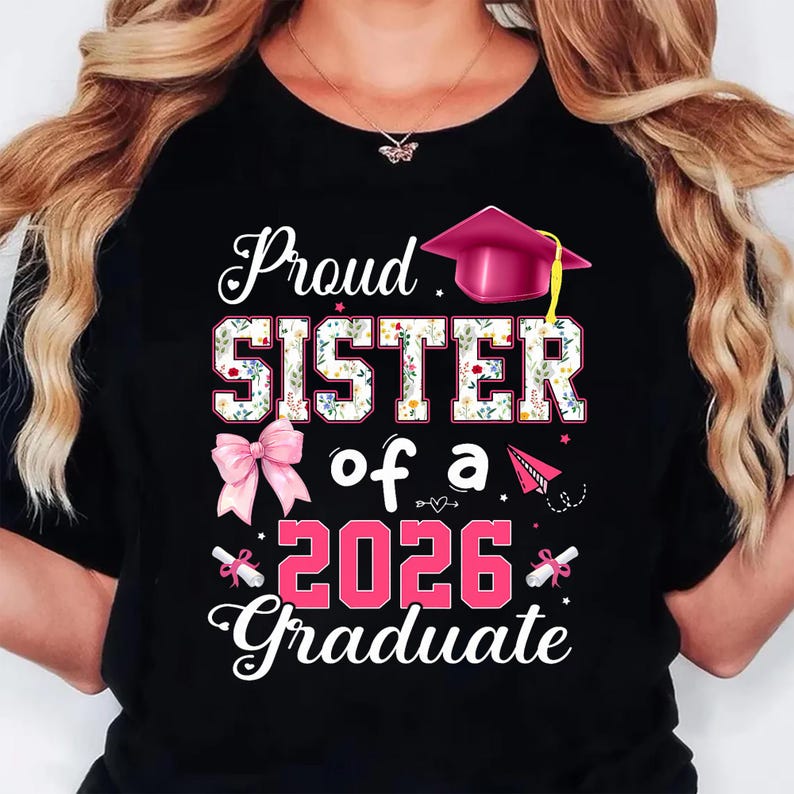 K&ouml;nnte beinhalten: Schwarzes T-Shirt mit dem Text "Proud SISTER of a 2026 Graduate". Das Wort "SISTER" ist mit einem floralen Muster gef&uuml;llt. Eine rosa Abschlusskappe und eine Schleife sind ebenfalls im Design enthalten.
