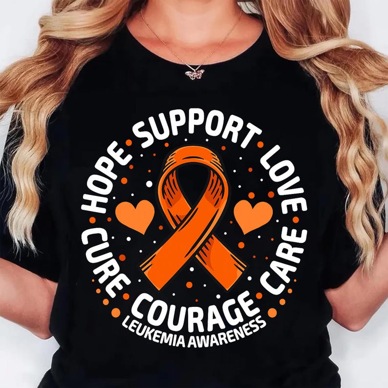 May include: Black t-shirt with an orange awareness ribbon, two orange hearts, and the words "HOPE, SUPPORT, LOVE, CARE, COURAGE, LEUKEMIA AWARENESS" in white. The design is circular and features white dots.