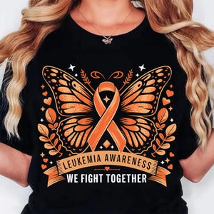 May include: Black t-shirt featuring a butterfly design with orange wings and an orange ribbon, symbolizing leukemia awareness. The text "LEUKEMIA AWARENESS WE FIGHT TOGETHER" is displayed on a banner below the butterfly.
