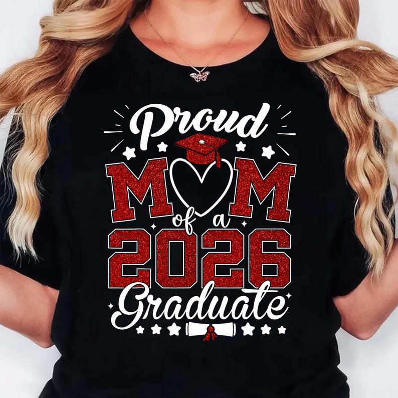 K&ouml;nnte beinhalten: Schwarzes T-Shirt mit einem roten Glitzer-Design mit der Aufschrift "Proud Mom of a 2026 Graduate". Das Design umfasst eine Abschlusskappe, Sterne und das Wort "Mom" in einem Herzen.