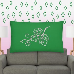 Op de afbeelding: Een groen kussen met een roze wijnstok- en bladontwerp. Het kussen ligt op een grijze bank.