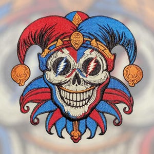 May include: Embroidered patch featuring a grinning skull in a jester's hat. The skull has lightning bolt eyes and is framed by red, blue, and gold details. The patch has a detailed, textured appearance.