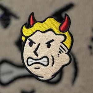 Puede incluir: Parche bordado con la imagen de una cara de dibujos animados con pelo amarillo, cuernos rojos y expresión enfadada. El parche tiene un borde negro, para ropa o accesorios.