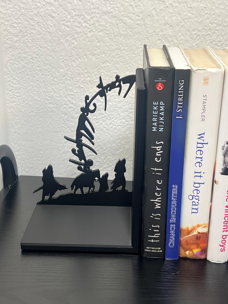 Op de afbeelding: Zwarte metalen boekensteunen met een silhouetontwerp van figuren te paard en lopend. De boekensteunen houden verschillende boeken vast, waaronder "This is Where it Ends" en "Chance Encounters".
