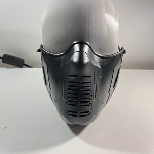 Puede incluir: Una máscara facial de plástico negro con un diseño geométrico y una serie de pequeños agujeros en la parte delantera.