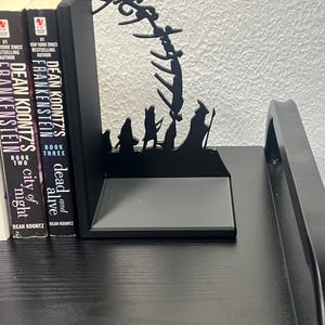 Op de afbeelding: Zwarte metalen boekensteunen met een silhouetontwerp met figuren en een gestileerde boog. De boekensteunen houden drie boeken vast met de titels "Frankenstein", "City of Night" en "Dead and Alive" van Dean Koontz.