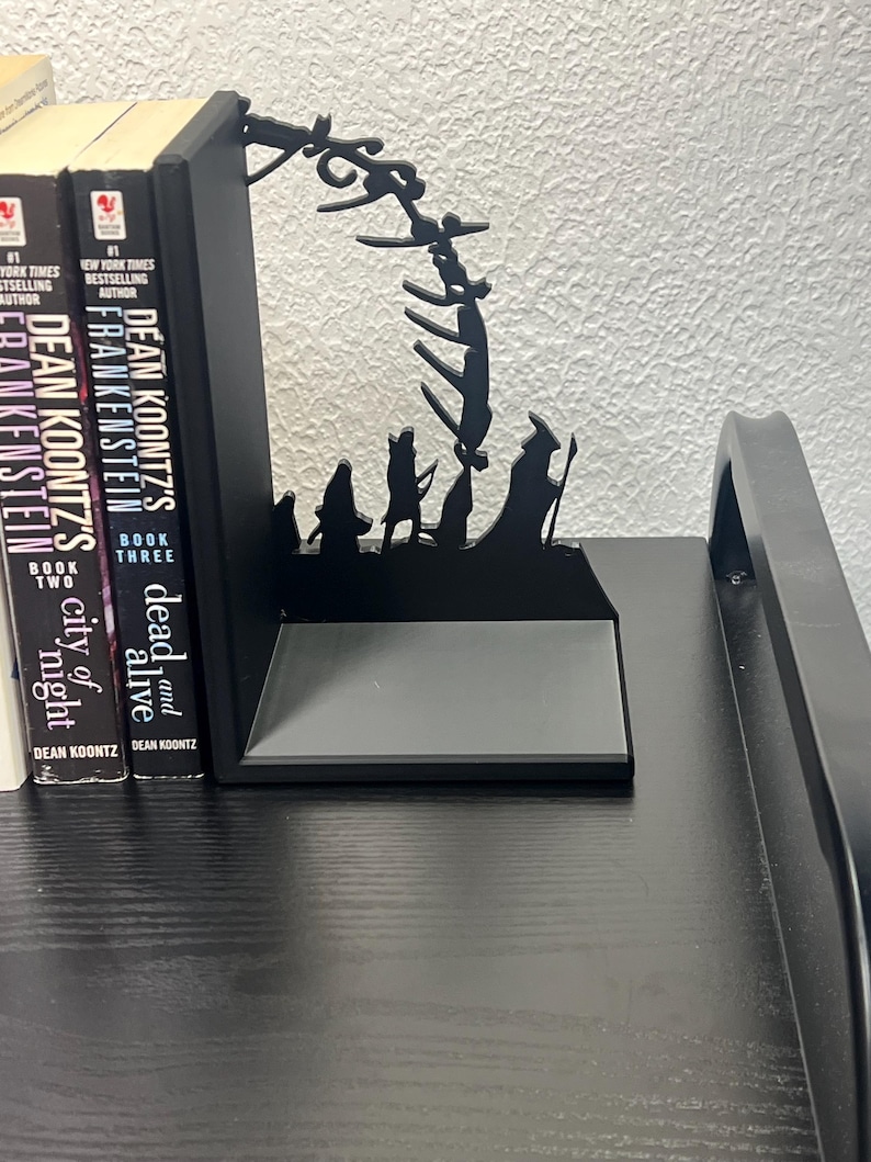Op de afbeelding: Zwarte metalen boekensteunen met een silhouetontwerp met figuren en een gestileerde boog. De boekensteunen houden drie boeken vast met de titels "Frankenstein", "City of Night" en "Dead and Alive" van Dean Koontz.