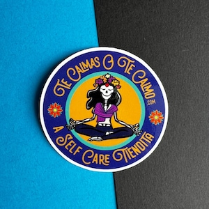 May include: A round sticker with a blue background and a yellow circle in the center. The circle features a skeleton figure in a purple shirt and blue jeans meditating with a flower crown. The text around the circle reads "Te Calmas o Te Calmo A Self Care Tiendita.com".