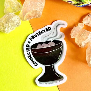 May include: A white sticker with black text that reads "Connected & Protected" and a black illustration of a chalice with smoke rising from it. The sticker is on a yellow and orange background. The text "tecalmasotecalmo.com" is at the bottom of the sticker.