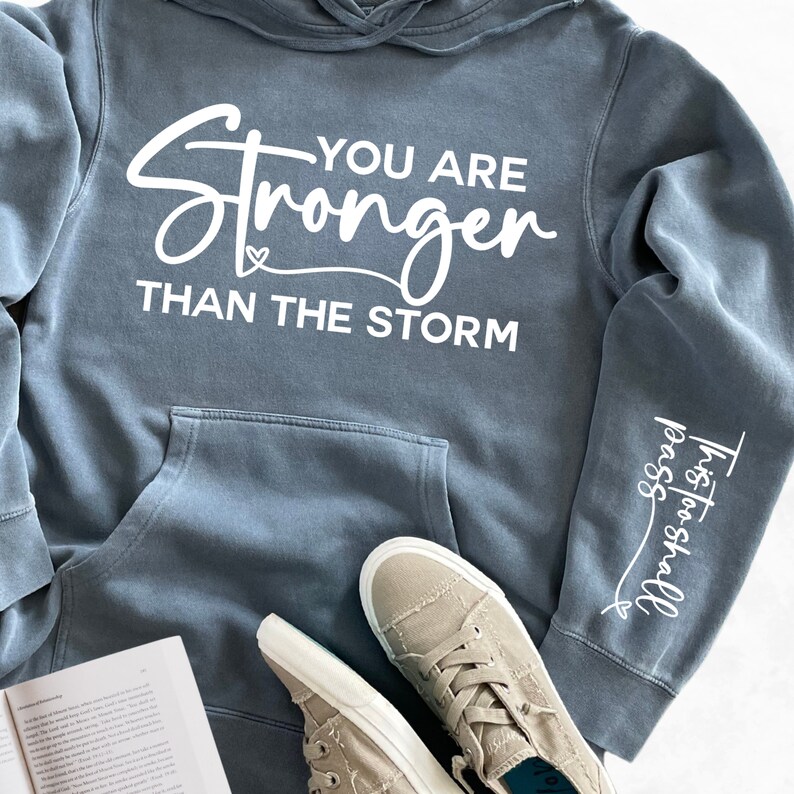 May include: A blue hooded sweatshirt with the text "You are Stronger Than The Storm" printed on the front and "This too shall pass" printed on the sleeve.