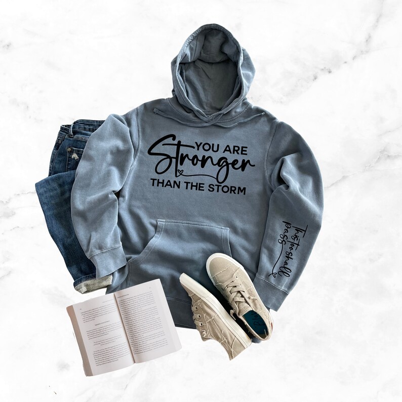 May include: A light blue hooded sweatshirt with the text "You are Stronger Than the Storm" printed on the front and "Trust in the Lord" printed on the sleeve.