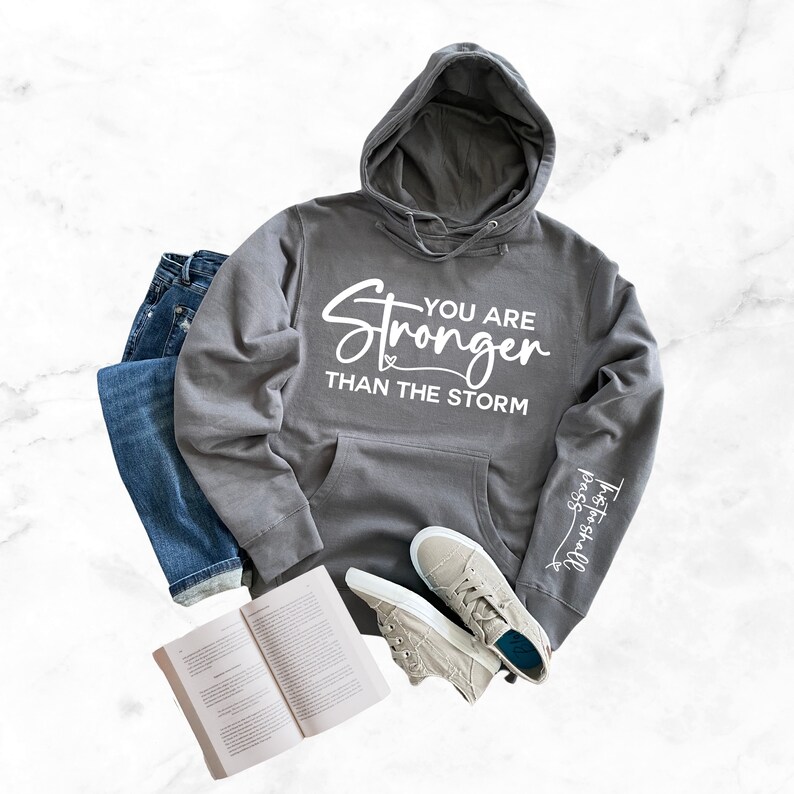 May include: A gray hooded sweatshirt with the text "You are Stronger Than The Storm" printed on the front and the text "Trust in the Lord" printed on the sleeve.