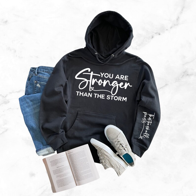 May include: Black hooded sweatshirt with the text "You are Stronger Than The Storm" on the front and "This too shall pass" on the sleeve.