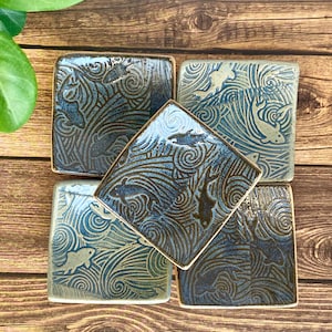 May include: Set of four square ceramic dishes with a blue and brown glaze. Each dish features a swirling wave pattern with fish silhouettes.