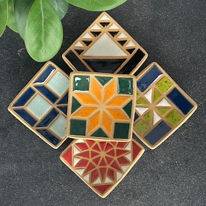 May include: Five ceramic square dishes with geometric patterns. The dishes are in shades of blue, green, yellow, orange, red, and white. The dishes are arranged in a circle with the points of the squares facing outward.