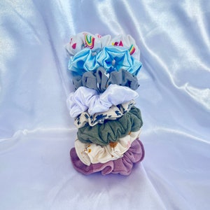 Pode incluir: Um conjunto de oito scrunchies coloridos em vários padrões e cores, incluindo branco, azul, verde e rosa. Os scrunchies são feitos de tecido macio e são perfeitos para segurar o cabelo no lugar.