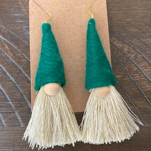 May include: A pair of green felt gnome earrings with white yarn tassels and wooden beads for noses.