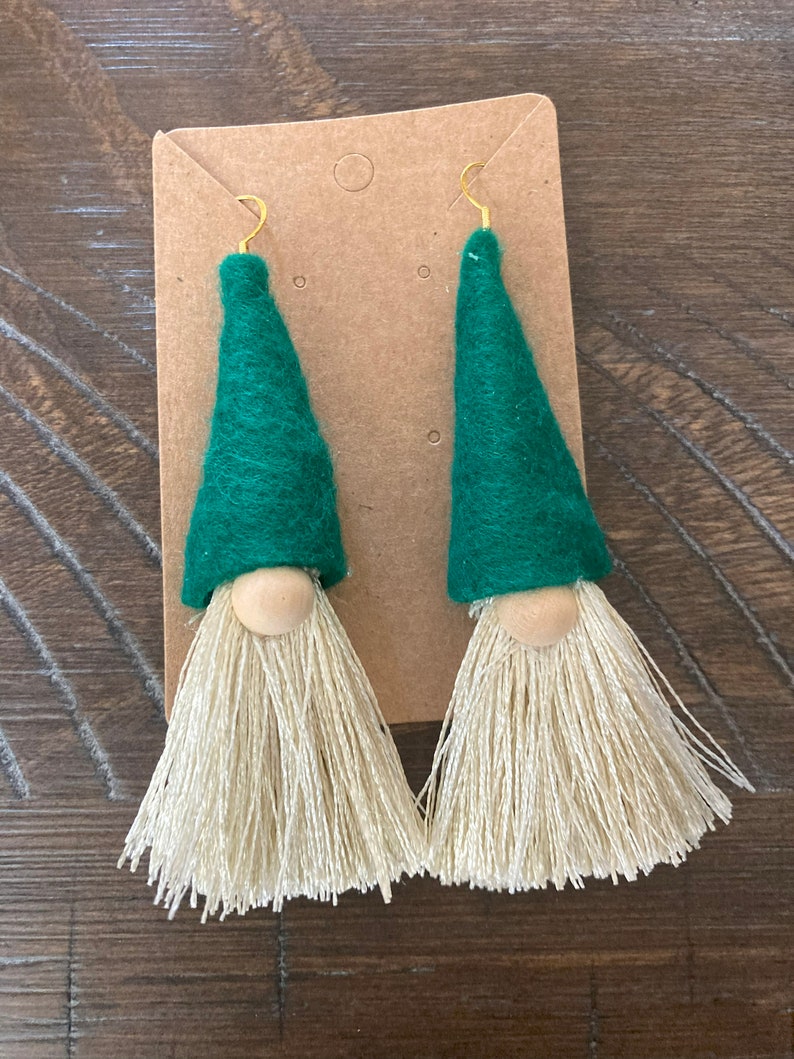 May include: A pair of green felt gnome earrings with white yarn tassels and wooden beads for noses.