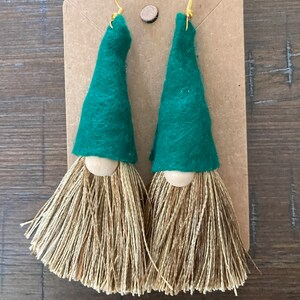 May include: A pair of green felt gnome earrings with brown yarn tassels. The earrings have wooden beads for the gnome's nose.
