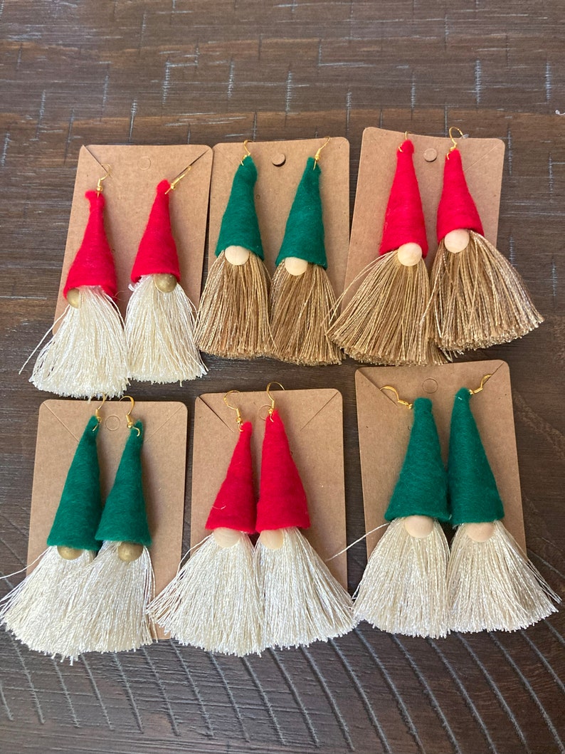 May include: Set of six pairs of gnome-themed tassel earrings. Each pair features a felt gnome hat in either red or green with a wooden bead face and a white tassel.