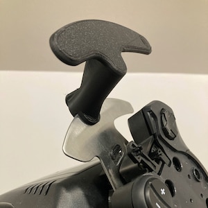 May include: A black plastic racing paddle shifter with a silver metal plate and a black knob with a plus and minus sign. The paddle shifter is attached to a black racing wheel.