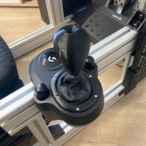 May include: Black gear shifter with a leather gear knob and a silver button with a "G" on it. The shifter is mounted on a silver metal frame.