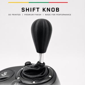 Op de afbeelding: Een zwarte 3D-geprinte pookknop met een gladde afwerking, bevestigd aan een metalen schacht en een zwarte lederen hoes. De tekst BALTIC MOTORSPORT SOLUTIONS SHIFT KNOB 3D PRINTED PREMIUM FINISH MADE FOR PERFORMANCE is zichtbaar met iconen.