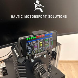 Könnte beinhalten: Ein schwarzes Fanatec-Rennsimulator-Setup mit einem Smartphone, das Renndaten anzeigt. Das Telefon ist über der Radbasis montiert. Der Bildschirm zeigt Motordaten, Rundenzeiten und andere Leistungskennzahlen an. Der Text "BALTIC MOTORSPORT SOLUTIONS" ist sichtbar.