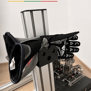 May include: A black racing glove with white geometric patterns resting on a black metal holder attached to a silver aluminum extrusion profile. The text BALTIC MOTORSPORT SOLUTIONS is visible at the top of the image in black and colored lines.