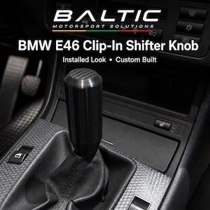 Può includere: Un pomello del cambio cilindrico nero con un motivo in fibra di carbonio sulla parte superiore, installato nell'abitacolo di un veicolo. Il testo BALTIC MOTORSPORT SOLUTIONS e BMW E46 Clip-In Shifter Knob Installed Look Custom Built è visibile.