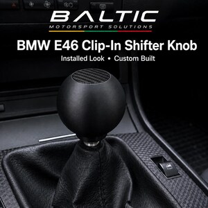 Può includere: Un pomello del cambio sferico nero con un inserto superiore in fibra di carbonio, installato su una cuffia del cambio in pelle nera. Il testo recita BALTIC MOTORSPORT SOLUTIONS, BMW E46 Clip-In Shifter Knob, Installed Look, Custom Built.