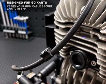 May include: A black RPM cable clip attached to a black cable on a go-kart engine. The text reads: BALTIC MOTORSPORT SOLUTIONS, RPM CABLE CLIP, DESIGNED FOR GO KARTS, KEEPS YOUR RPM CABLE SECURE AND IN PLACE, CLEAN INSTALLATION, DURABLE 3D PRINTED, FITS MOST KART SETUPS, EASY INSTALLATION, BUILT BY ENTHUSIASTS. FOR RACERS.